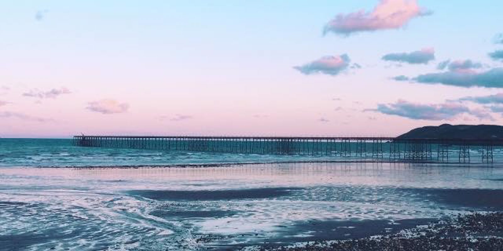 A picturesque photo of Ramsey Bay showing pink and blue clouds, a calm sea and the pier in the background