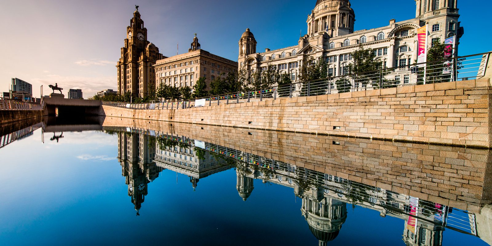 The Three Graces of Liverpool at Pier Head, with the blue sky reflecting off the water