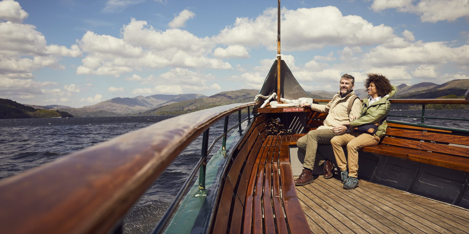 A male and female couple sat on a wooden boat in the Lake District