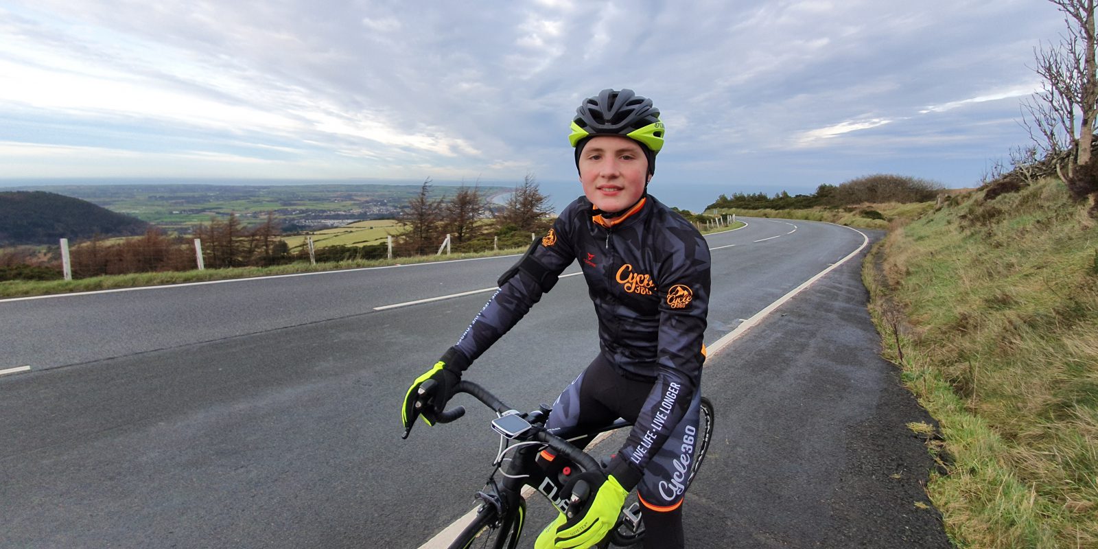 Jake Hodgson posing on his pedal bike with full cycling outfit and helmet on Isle of Man road