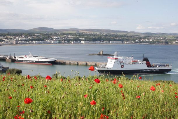 A photo taken from Douglas Head which features Steam Packet Company vessel Ben-my-Chree sailing into Douglas Harbour with Manannan already in bay. Red poppies and green grass in the foreground