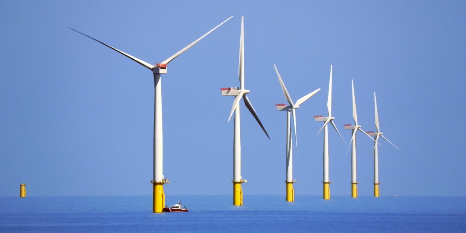 Six white and yellow wind farms at sea with a ship at one