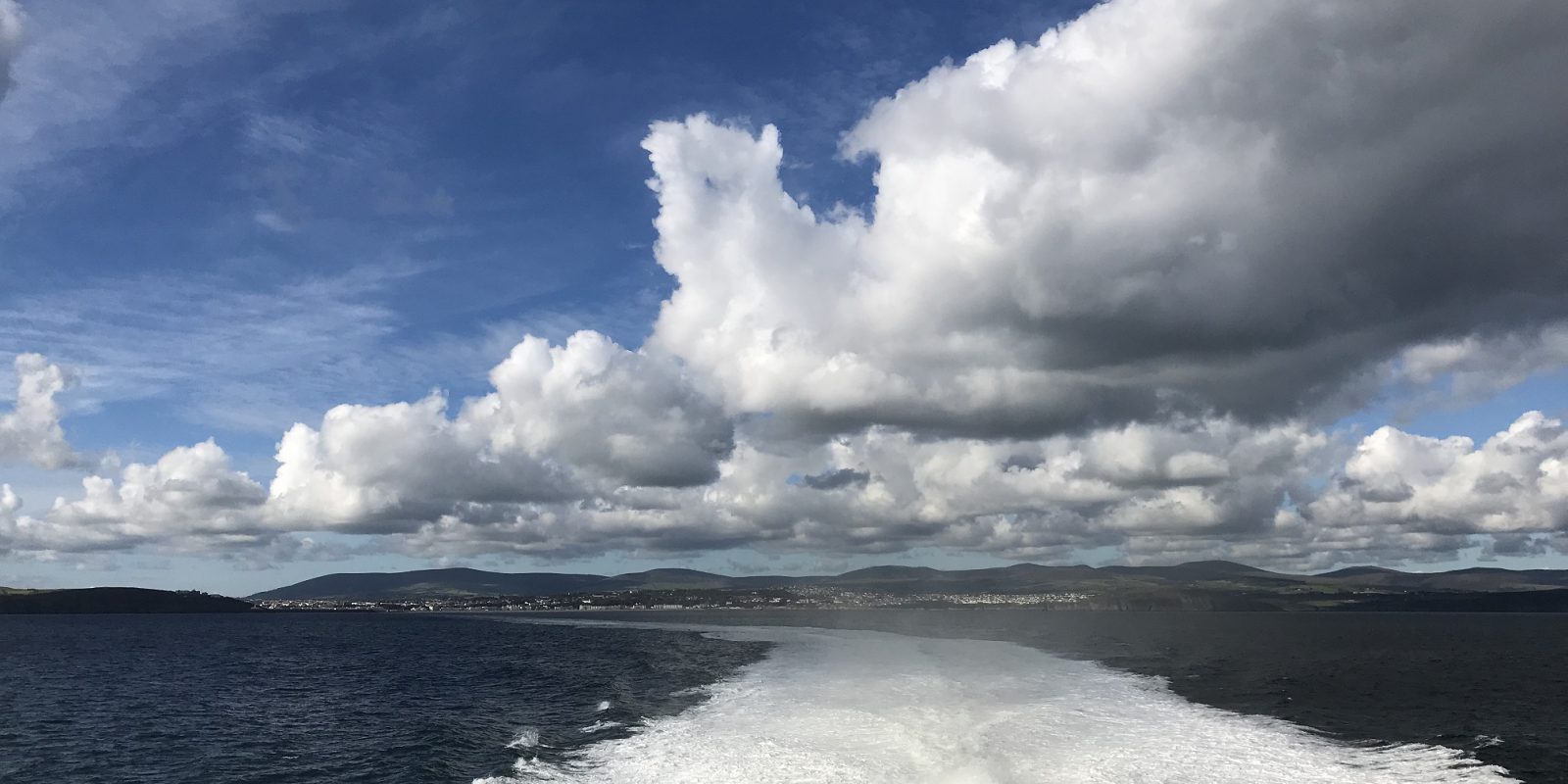 View of the blue sea, sky and clouds from the back of the vessel with the Isle of Man’s coast in the distance