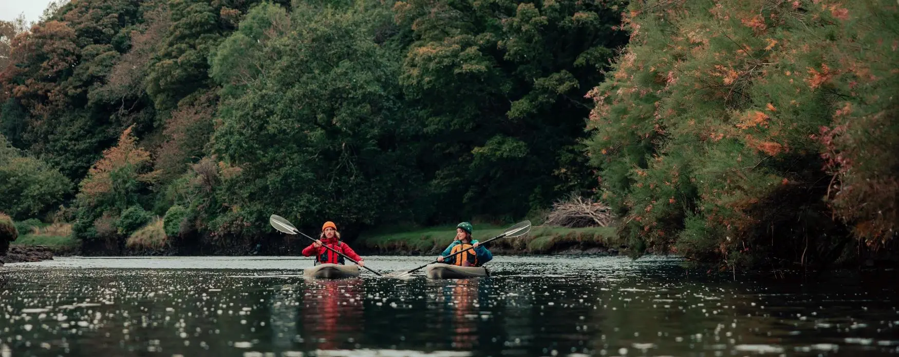 A couple kayak down a river in the Isle of Man in autumn.